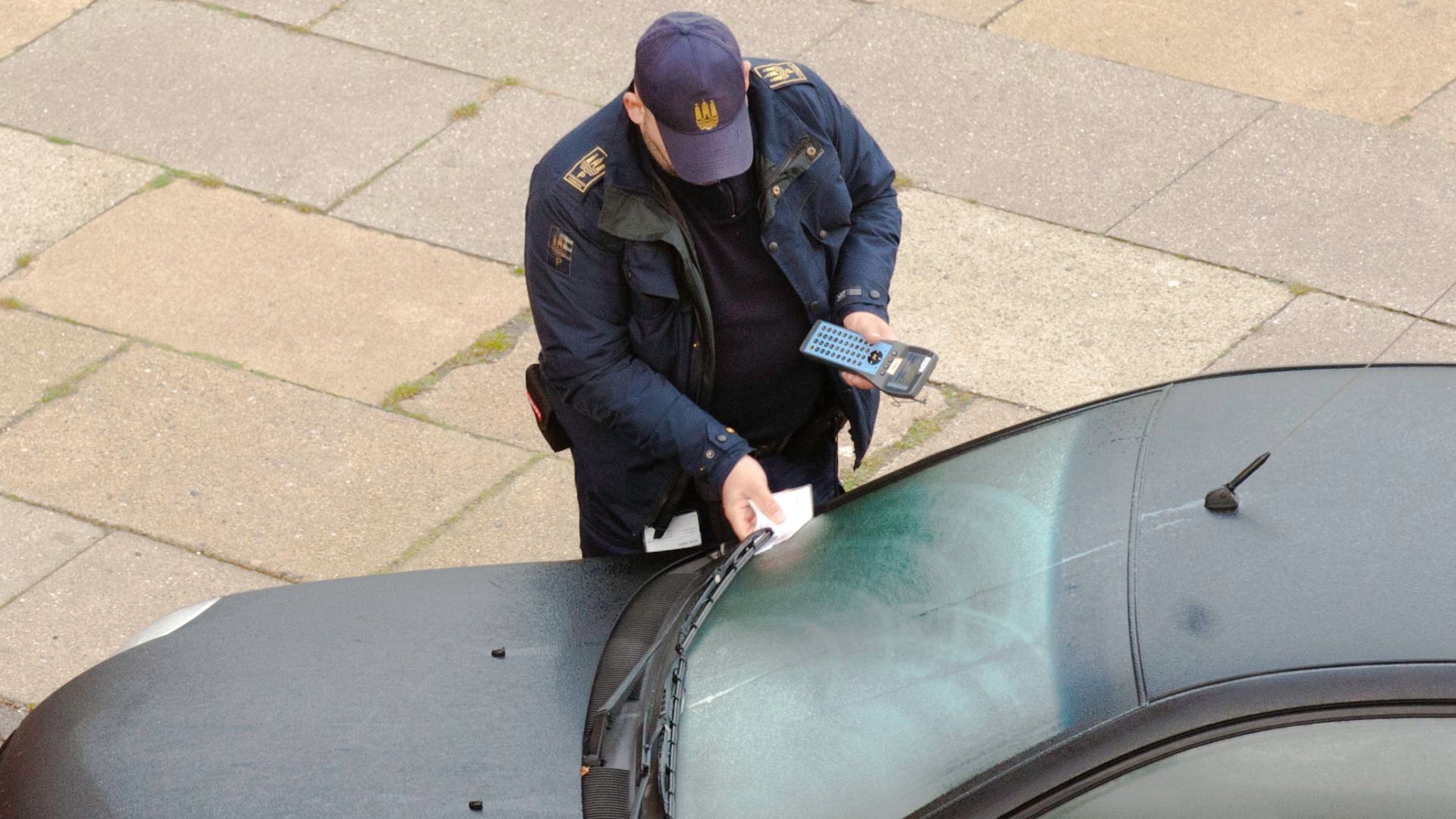 A serviceman from the Parking Department of Copenhagen Municipality, delivering a parking fine (put under the wiper) on an illegal parked car.