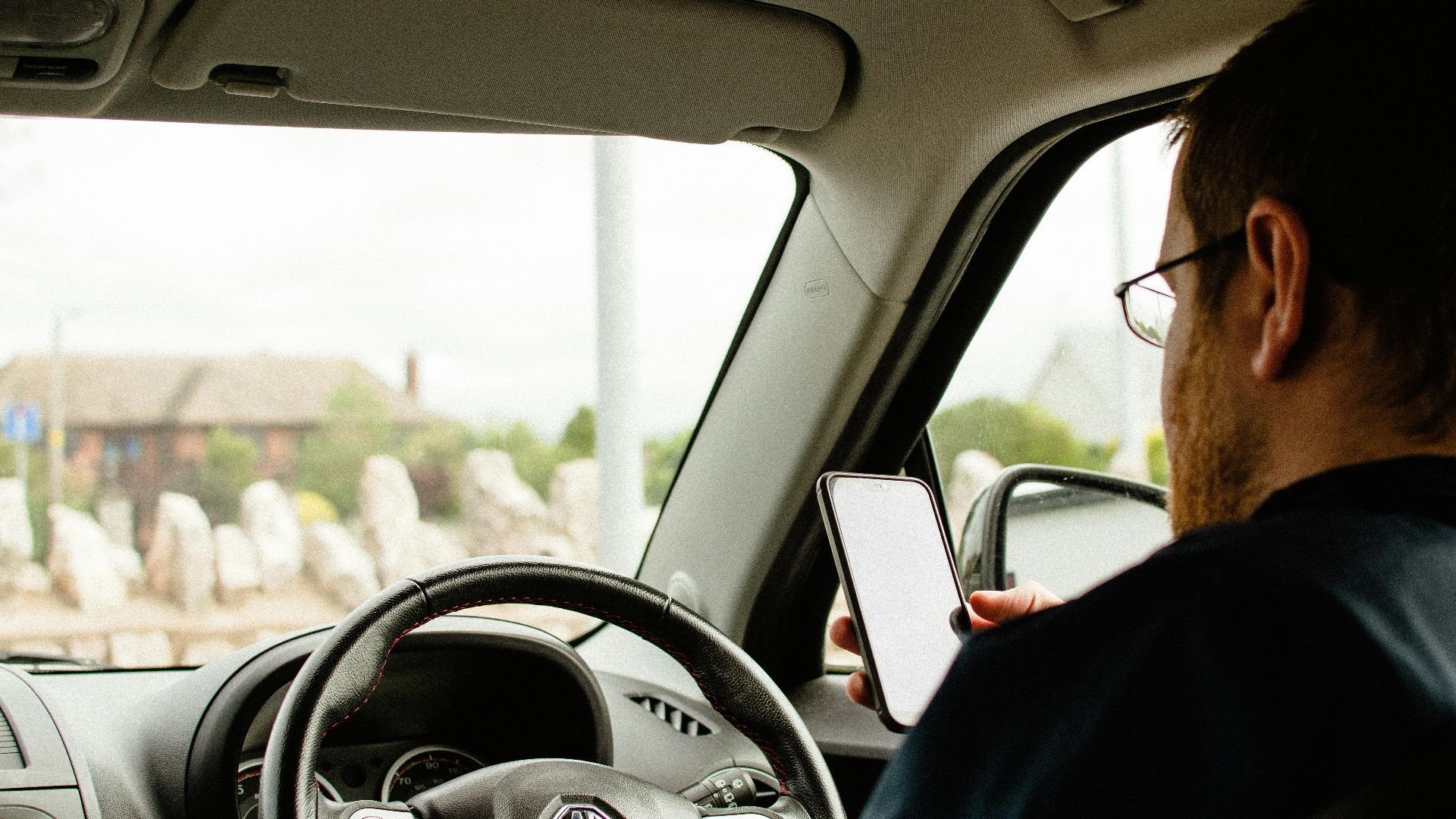 Back view of anonymous male in casual clothes sitting in car behind wheel and using smartphone