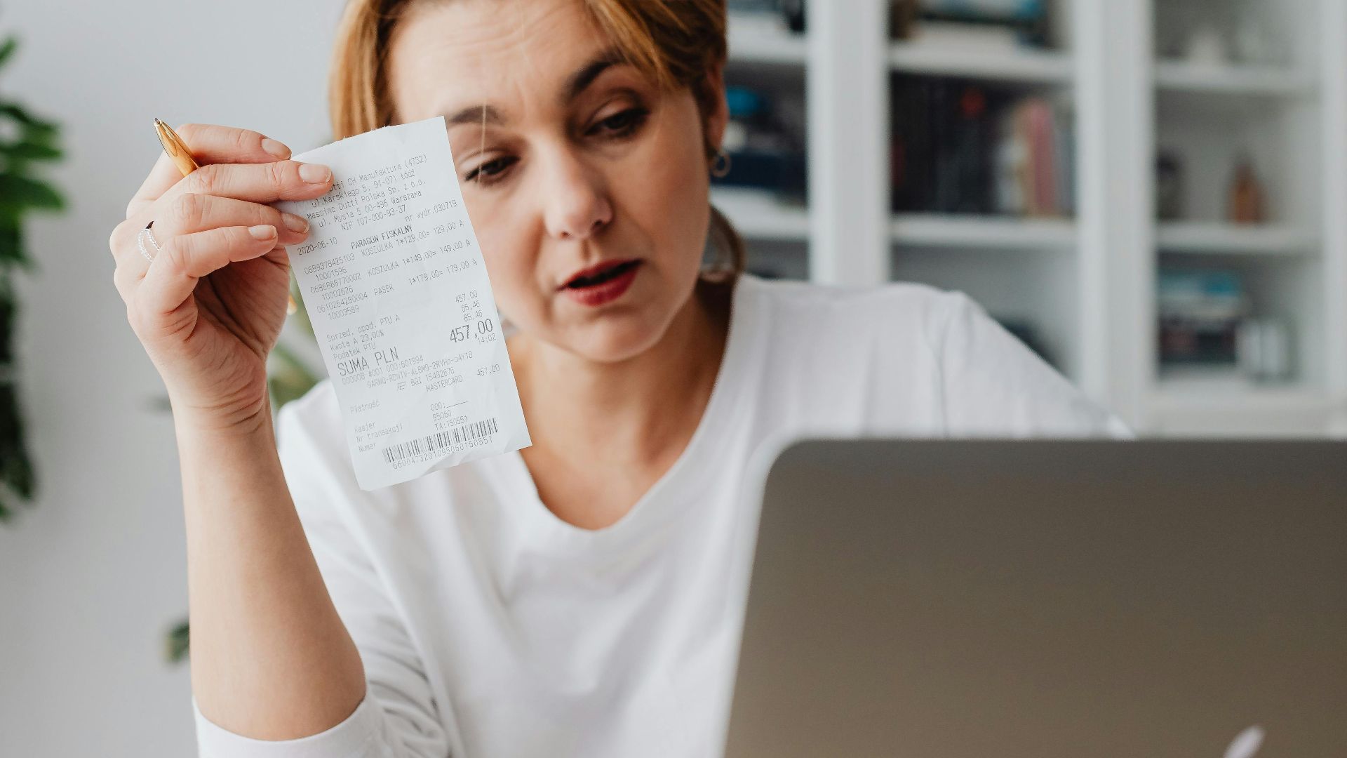 Woman using laptop while managing finances with receipts and cash on the table.