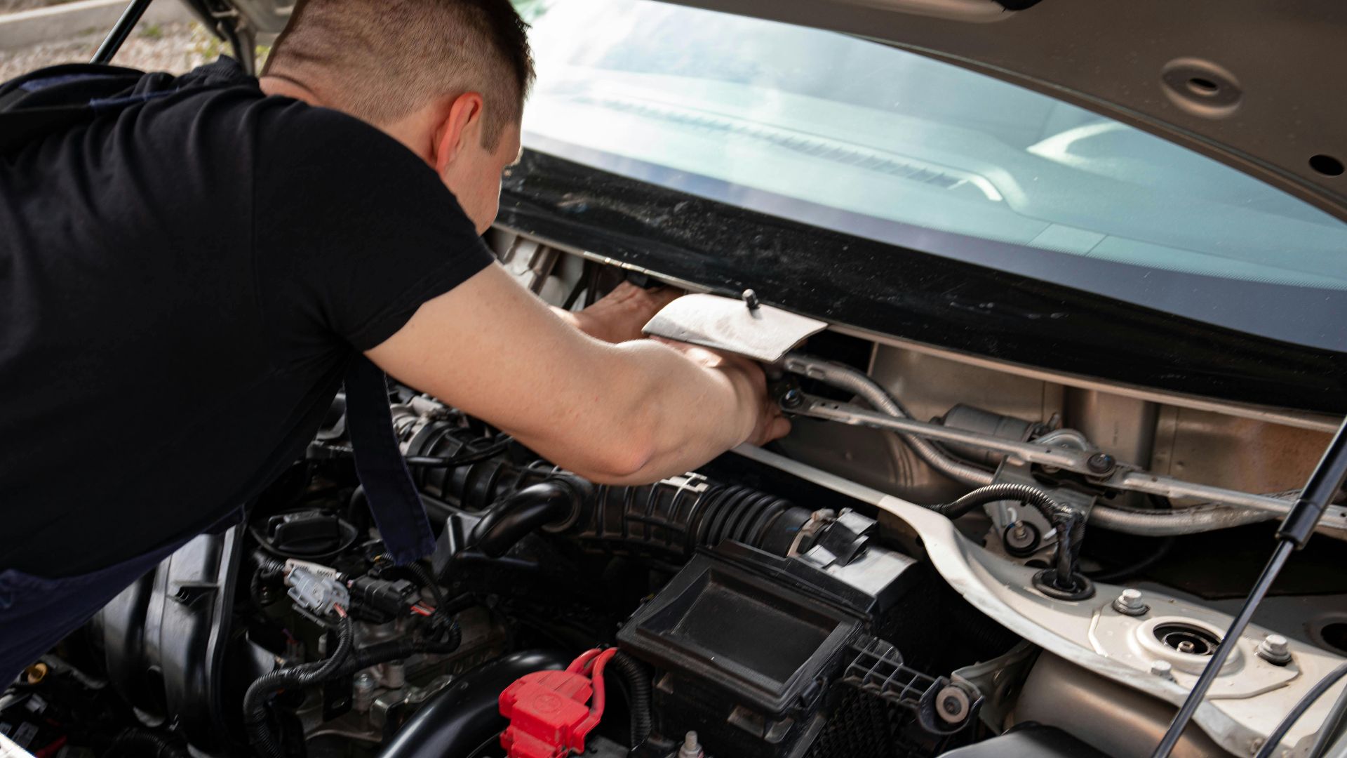 A mechanic busy repairing an engine under the hood of a car in a garage setting.