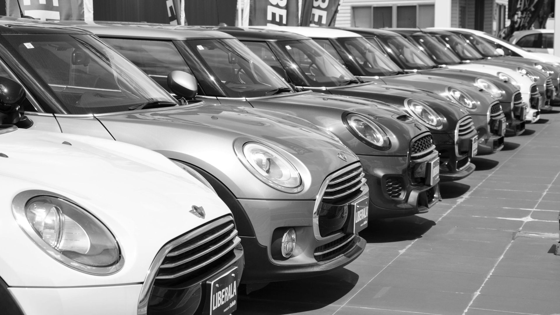 Black and white photo of a row of Mini Cooper cars parked outdoors in a car dealership.