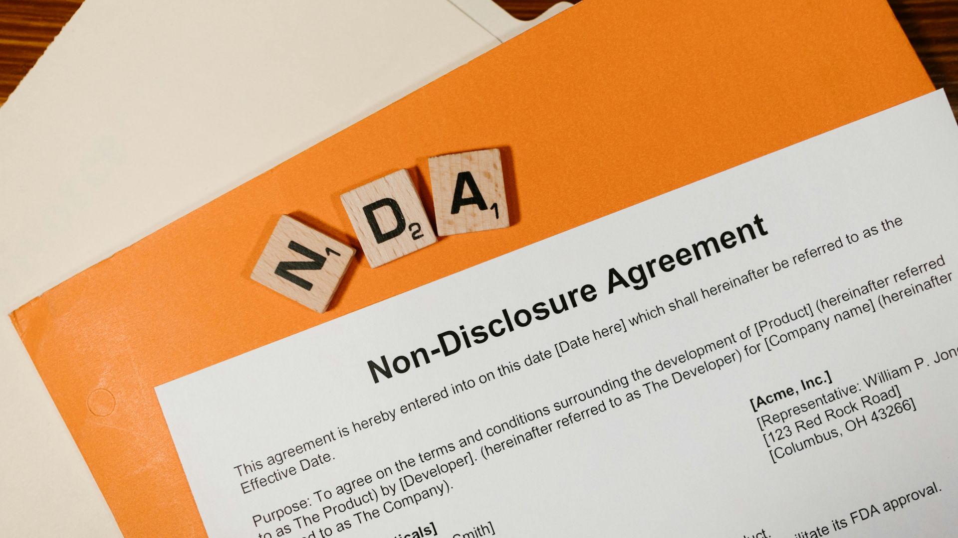 Top view of a Non-Disclosure Agreement with NDA in Scrabble tiles, emphasizing confidentiality.