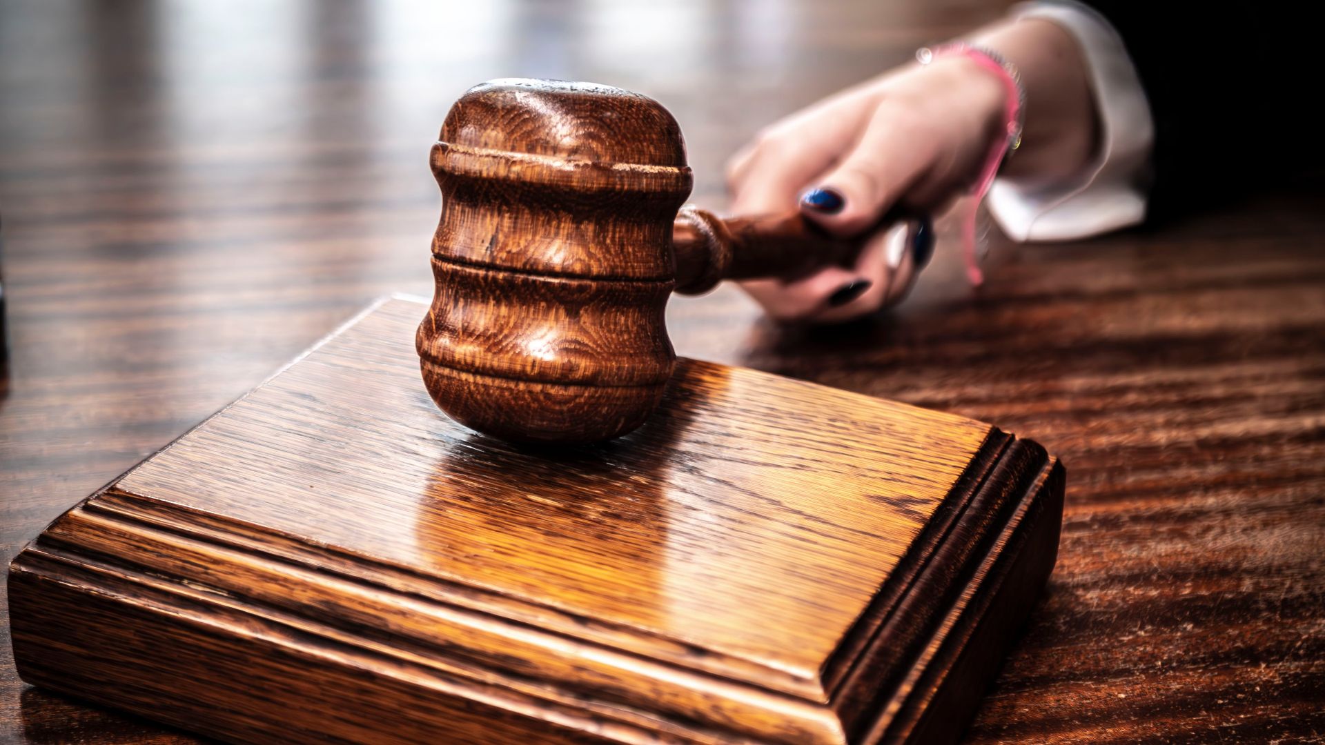 Close-up image of a wooden gavel held by hand on a desk in a courtroom setting.