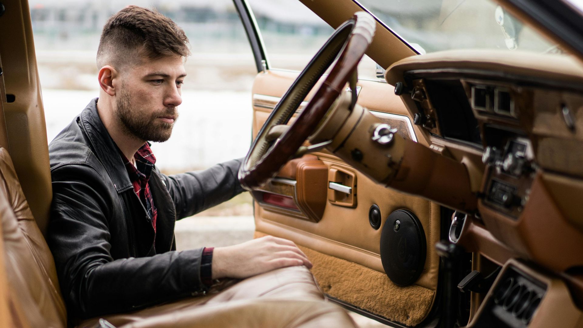 Confident adult man in leather jacket and shirt getting on driver seat of car on street in daylight