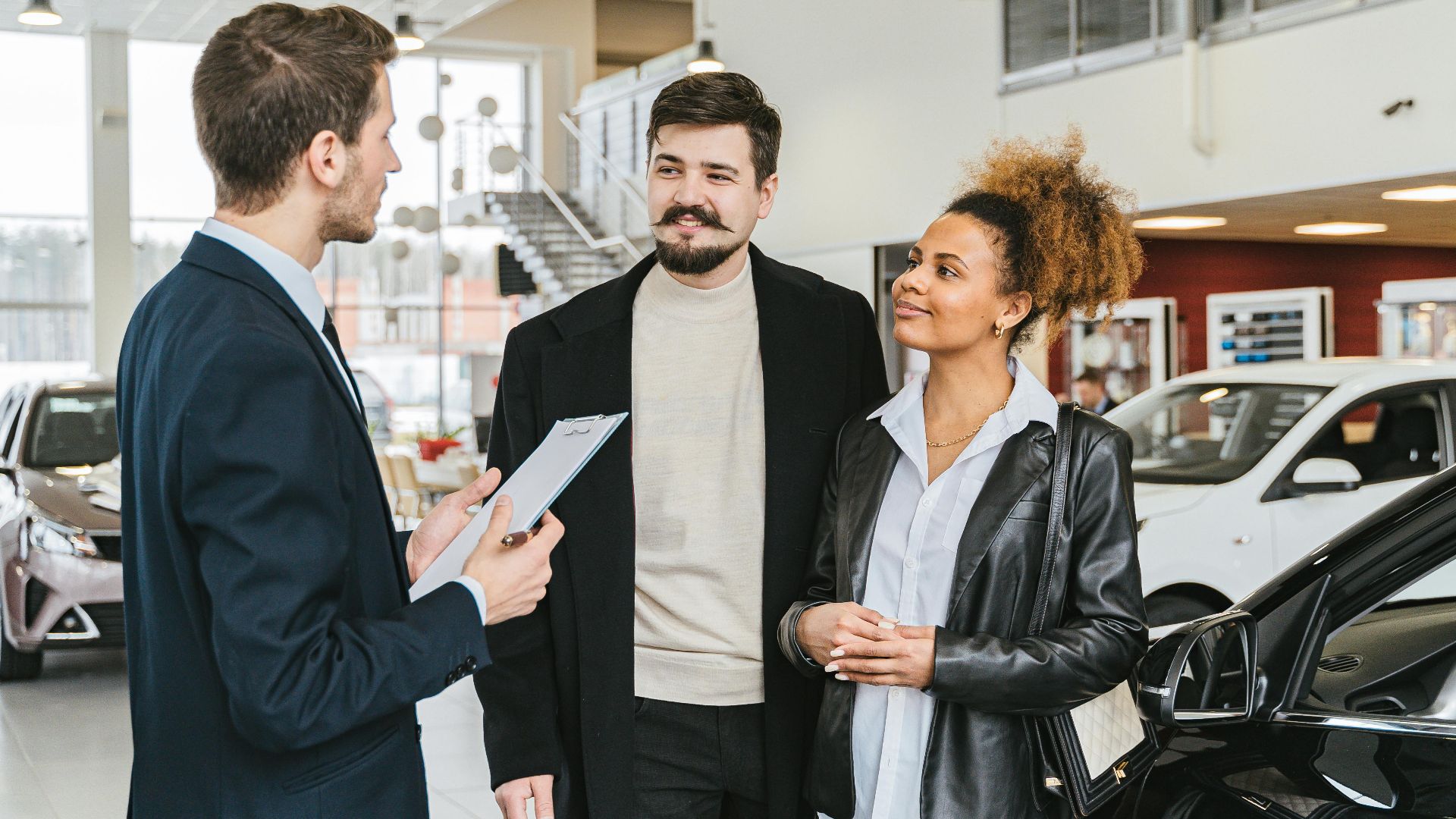 Couple discussing car purchase with salesman at indoor dealership, engaging conversation.