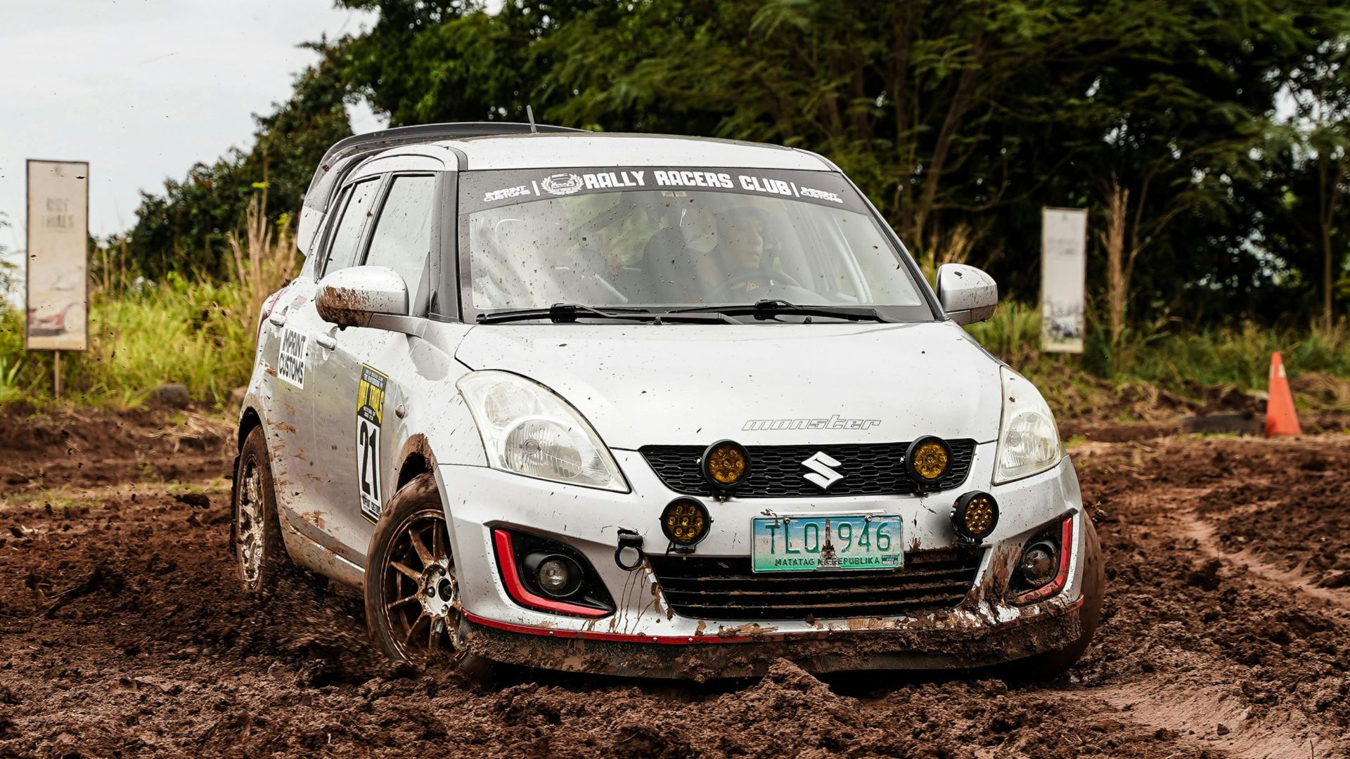 A white rally car in action on a muddy course, captured outdoors during daytime.