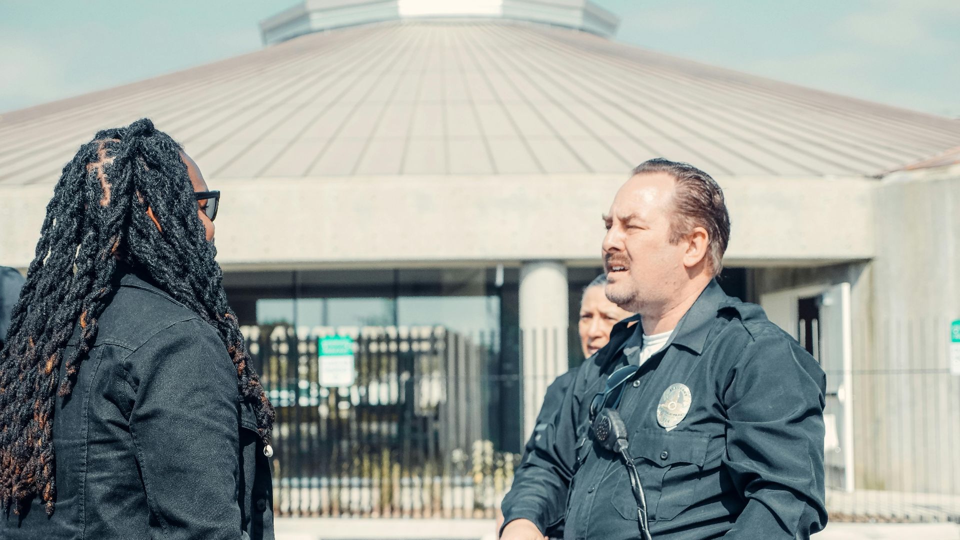 Police officers interacting with a civilian outside a public building, emphasizing community relations.