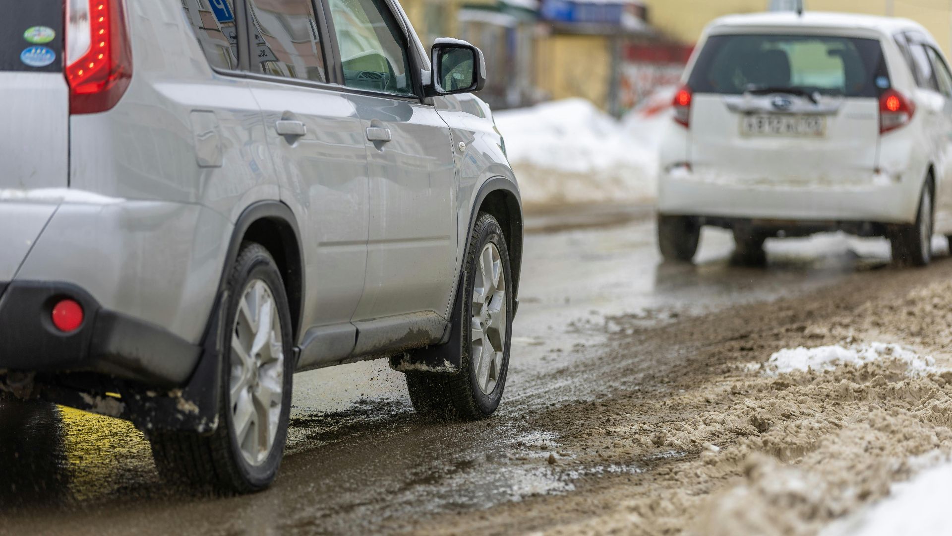 Two cars driving cautiously on a slushy, snowy road during winter.