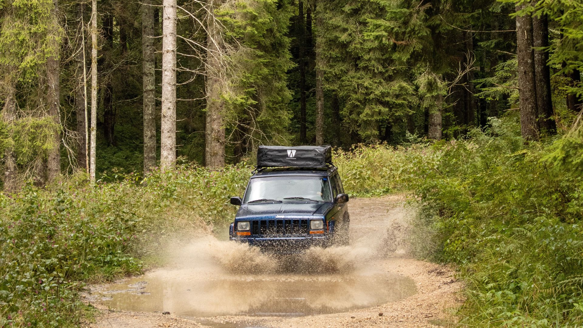 4x4 vehicle splashing through a muddy trail in a dense forest in Asiago, Italy.