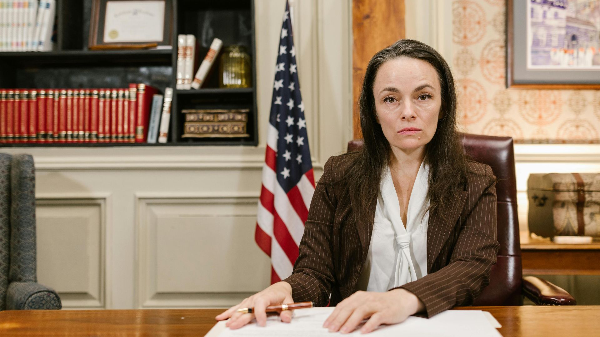 Confident female lawyer at her desk in a law office with legal books and the American flag.