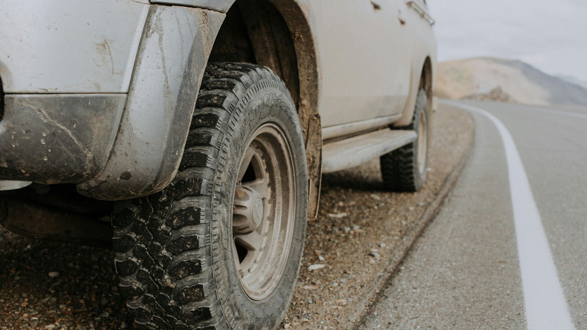 A rugged off-road vehicle's dirty tire on a gravel roadside in Altai Republic, Russia.