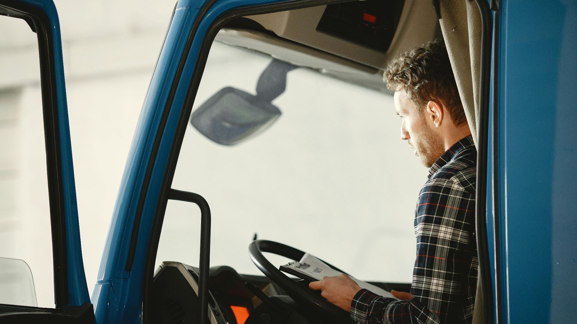 A man sitting in a truck cabin reading a document inside a blue truck, showcasing focused driving preparation.