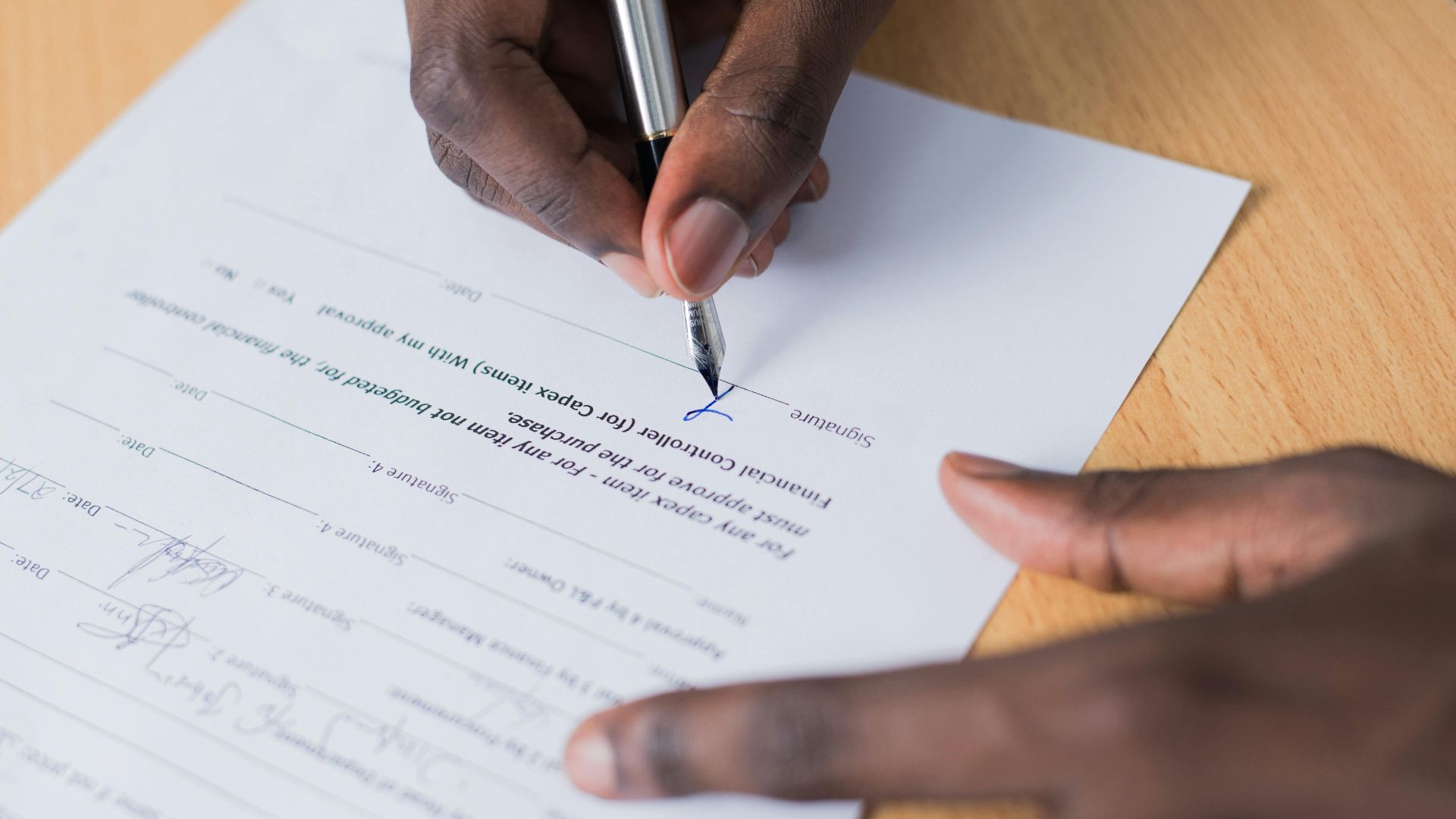 A close-up view of a person's hand signing a business contract on a desk with a pen.