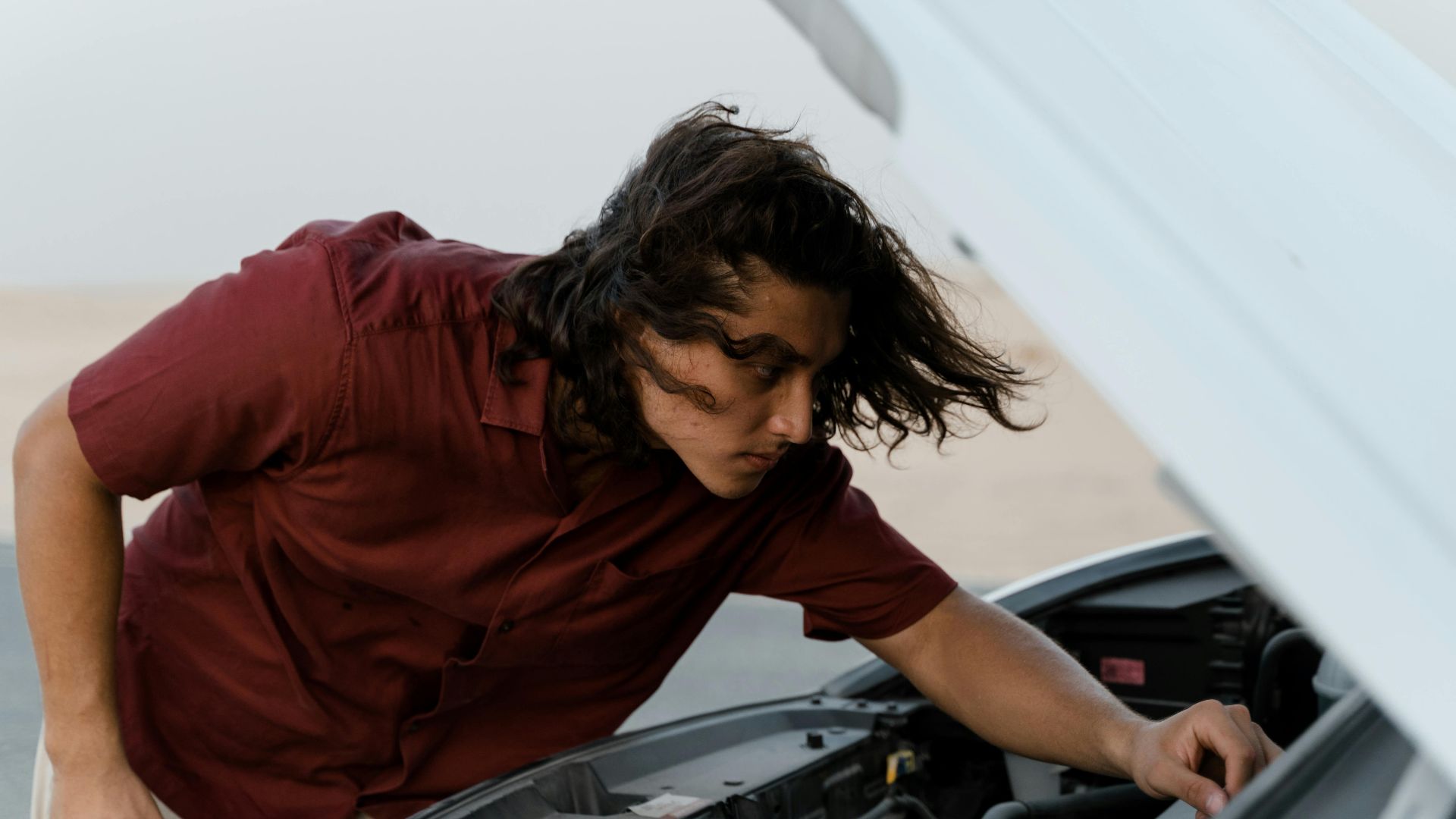 Person checking under the hood of a car for maintenance outdoors on a bright day.