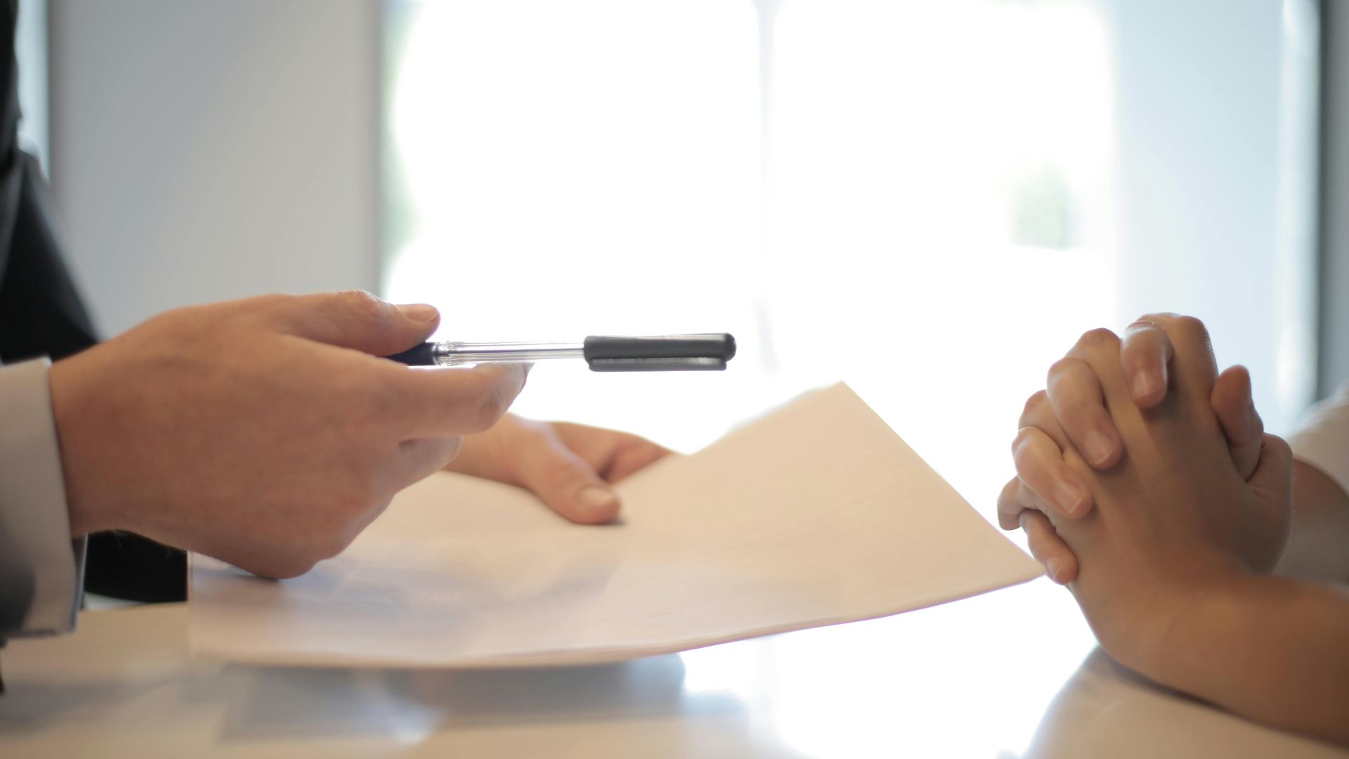 Side view of faceless formal man giving pen and paper to focused female with clenched hands at table on meeting