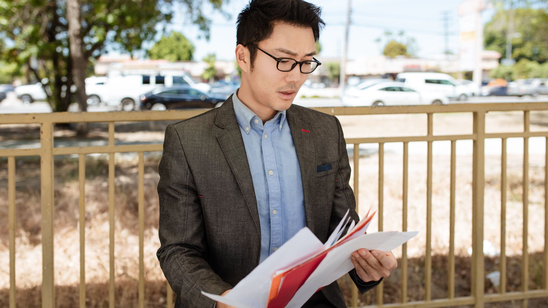 Asian businessman in a suit checking documents outdoors on a sunny day.