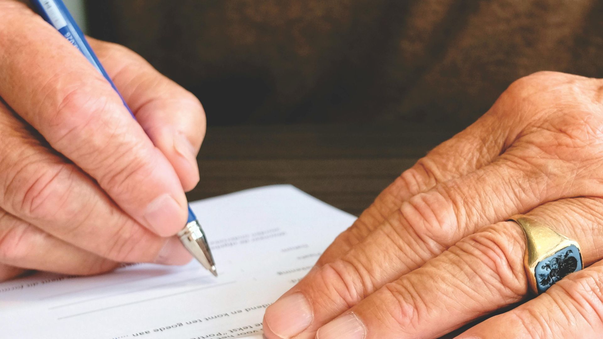 Close-up of a senior adult signing a legal document with a focus on hand and gold ring.