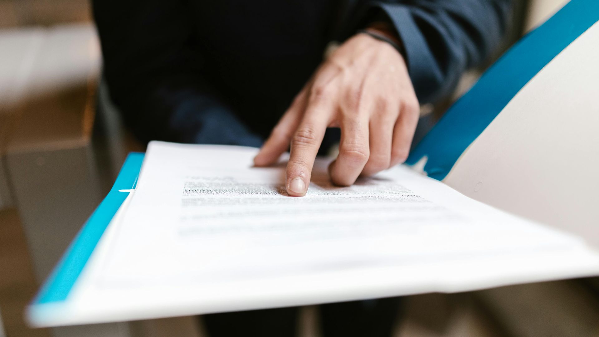 Close-up of a hand pointing at text on a business document in an office environment.
