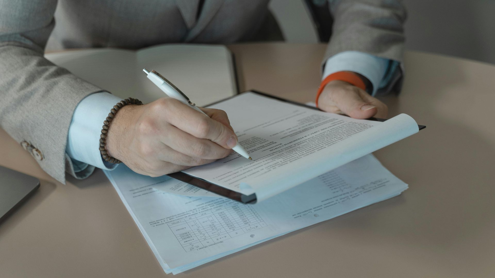 Close-up of business person signing documents at a desk with a pen.
