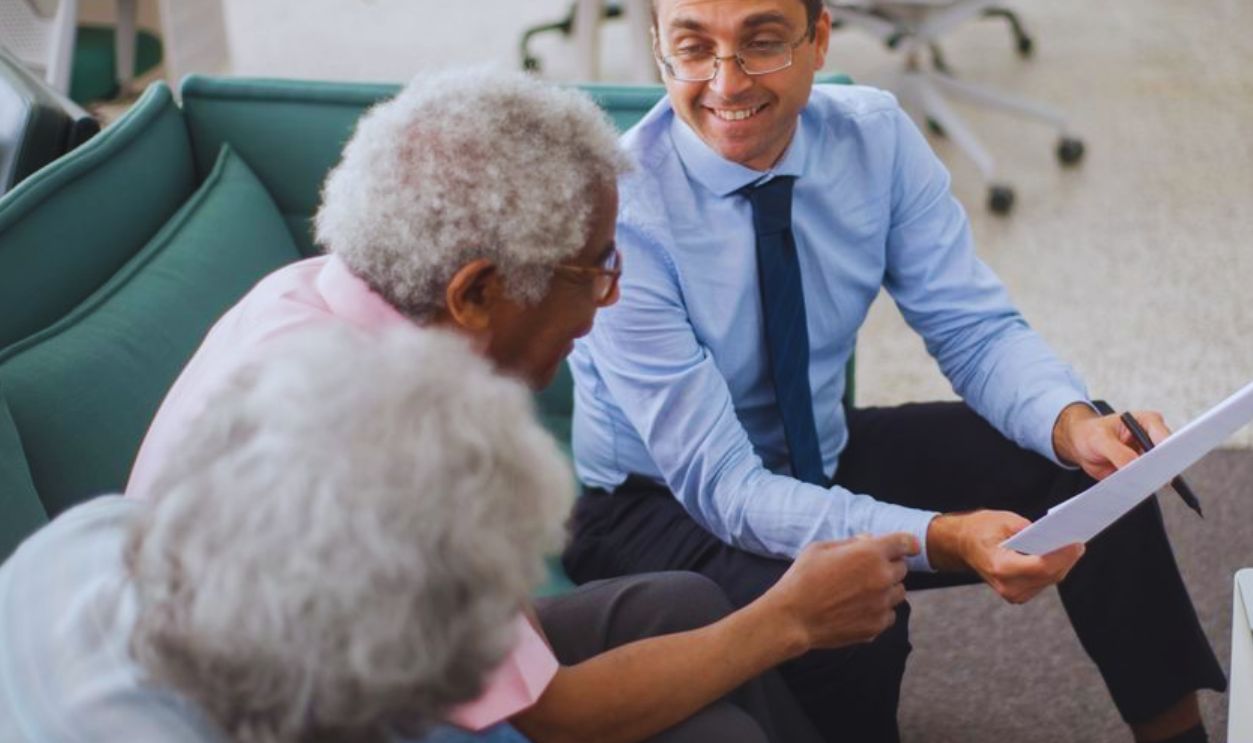 Consultant discussing financial plans with senior clients in a modern office setting, using documents and a laptop
