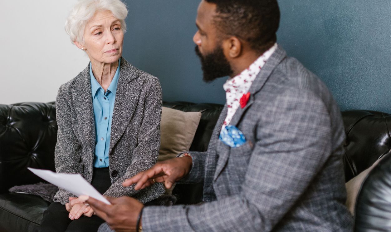 An elderly woman and a man in a professional meeting discussing documents indoors