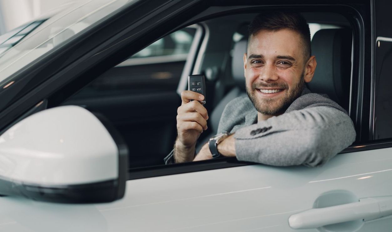 Happy young man holding car keys inside a vehicle. Perfect image for car rental or sales