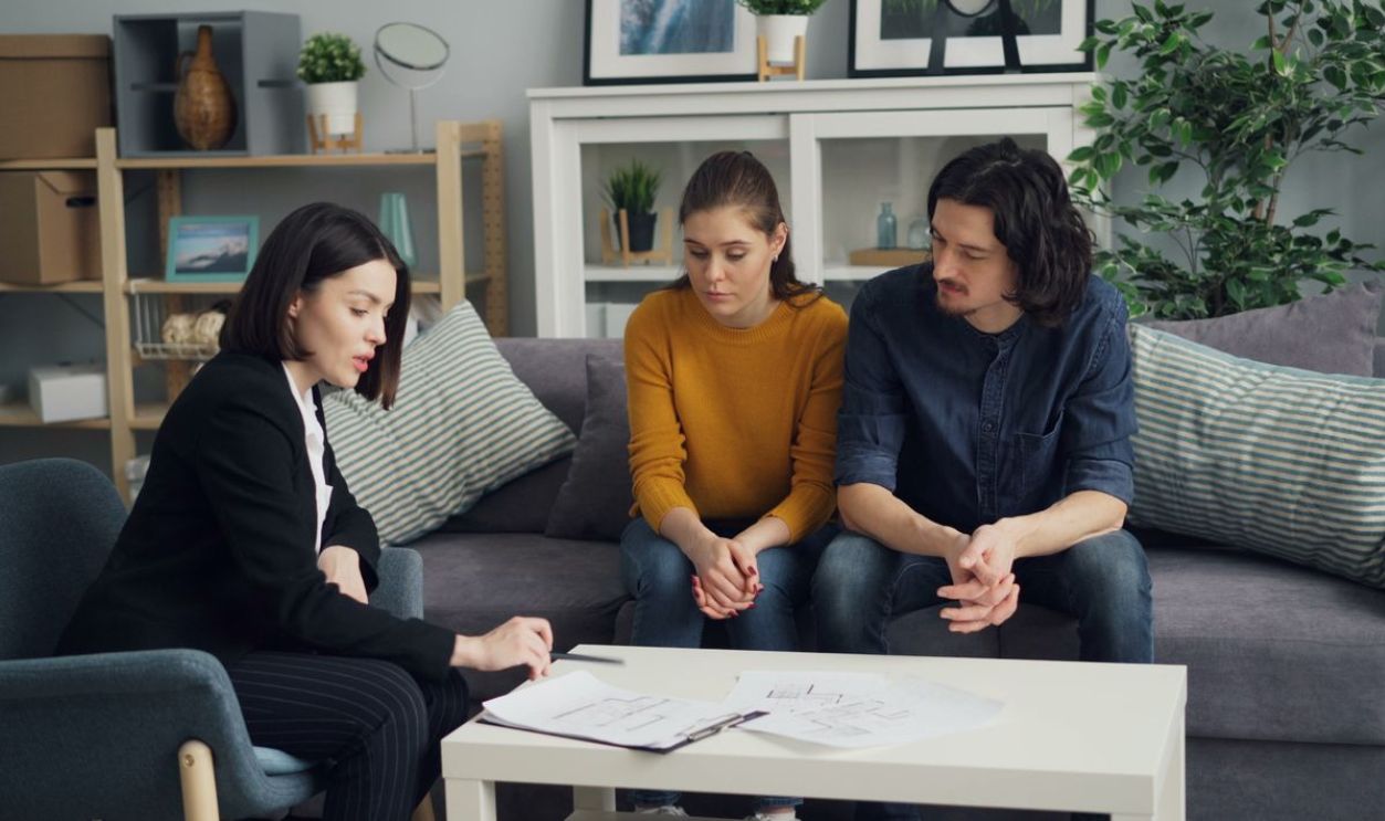 Couple discussing property with real estate agent in cozy living room setting, reviewing documents