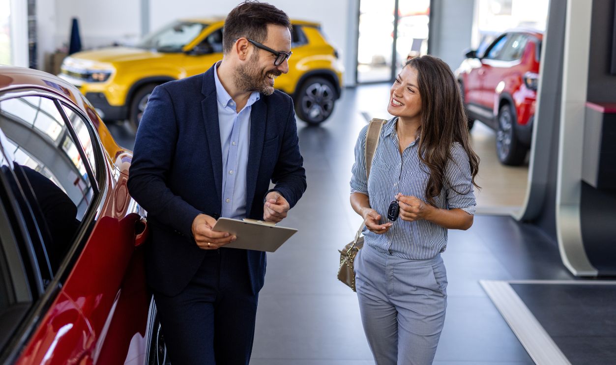 Beautiful young woman is talking to handsome car dealership worker while choosing a car in dealership
