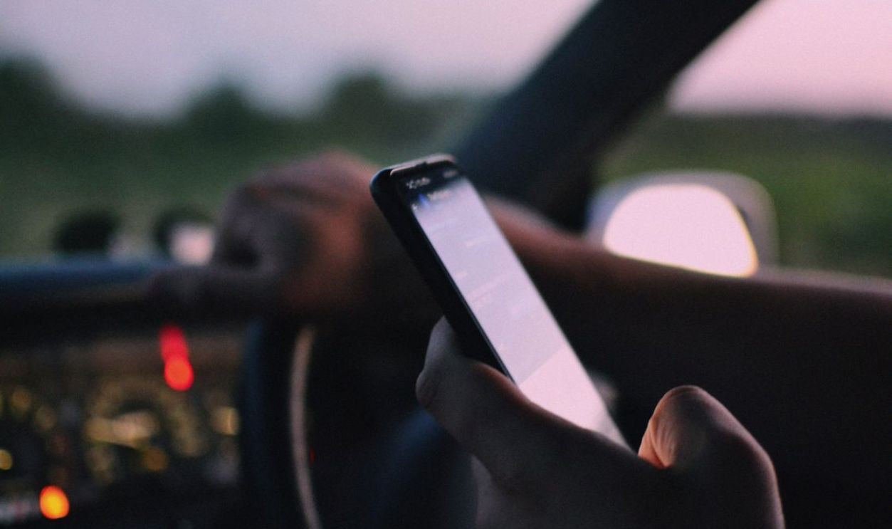 Close-up of a person using a smartphone while driving in a car at dusk.