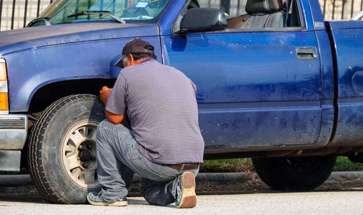 A man attentively repairing a flat tire on a blue truck in sunny Houston, Texas.