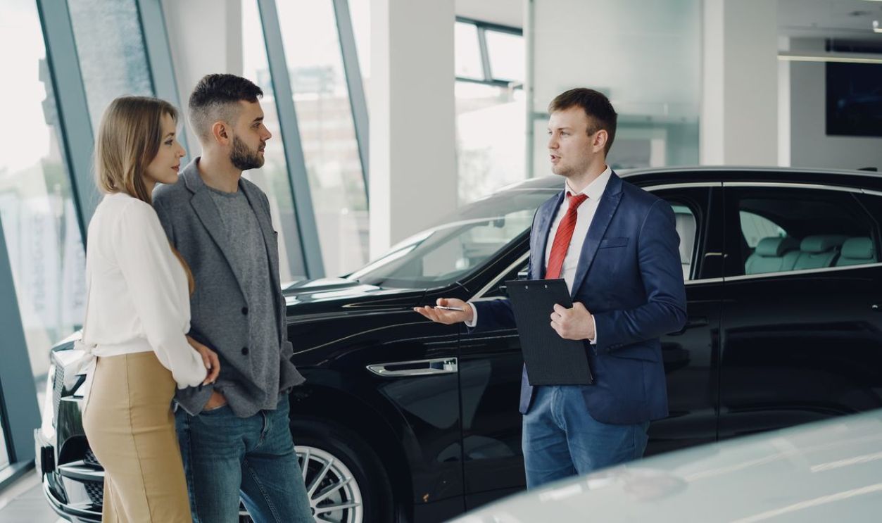 A couple talks with a salesman in a modern car showroom, considering a vehicle purchase