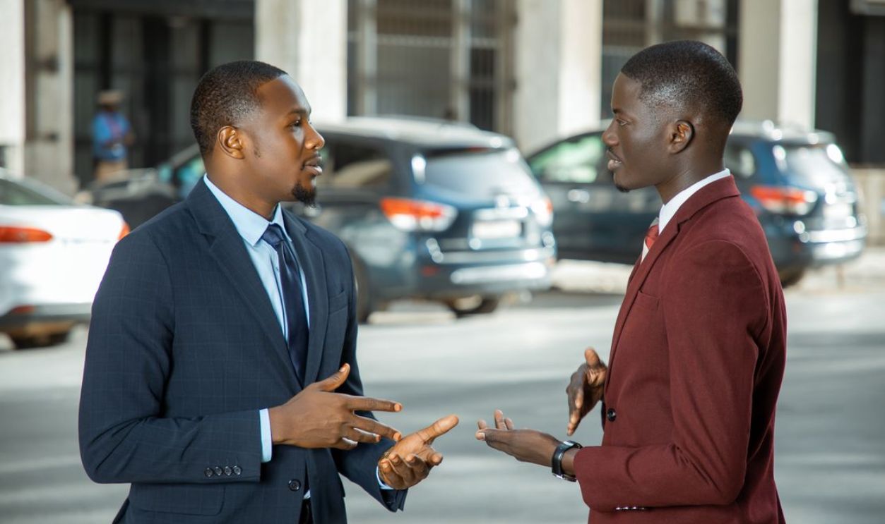 Two African businessmen in formal suits have a discussion on a city street in Dakar, Senegal