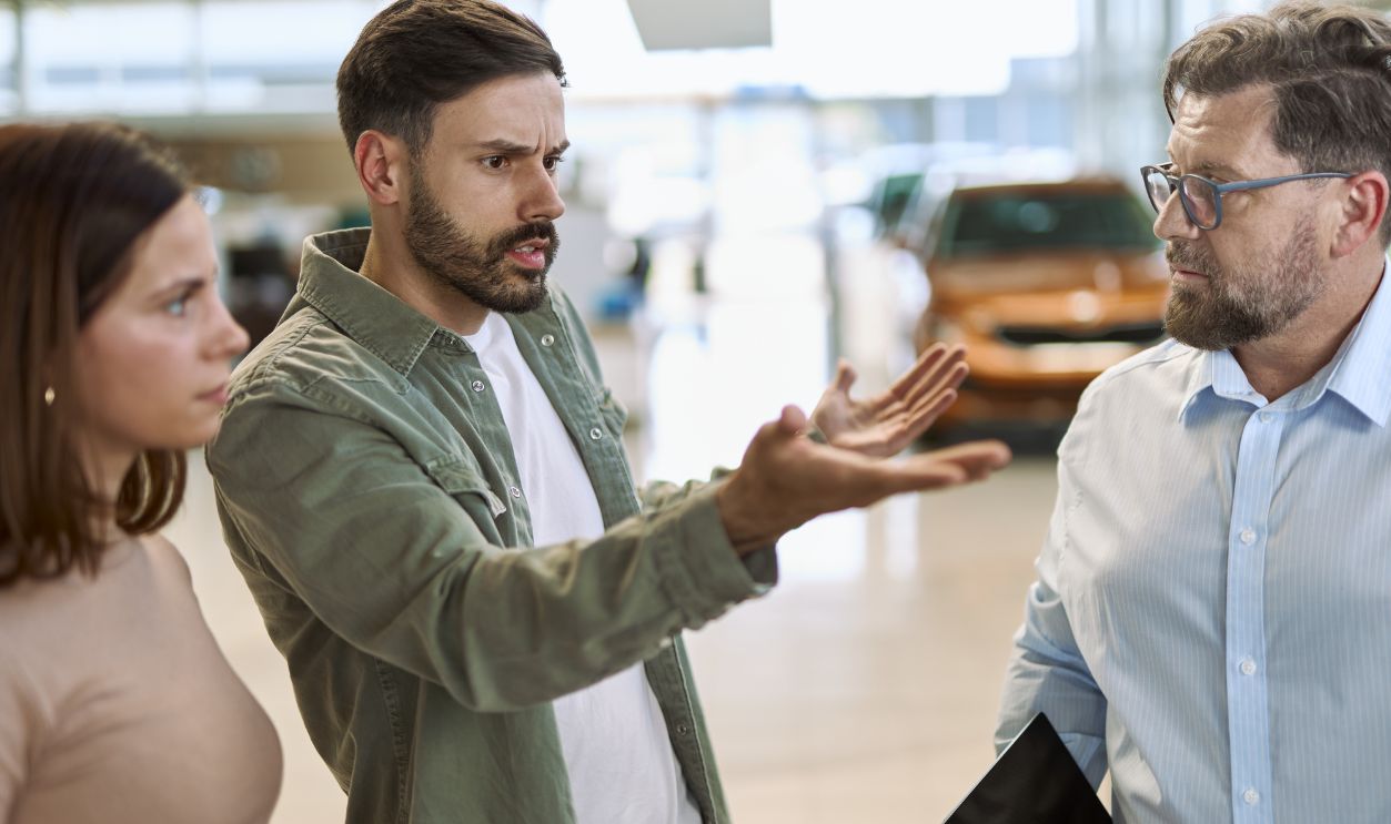 Shutterstock-2630721447, Displeased man and his wife arguing with car salesperson in a car showroom.