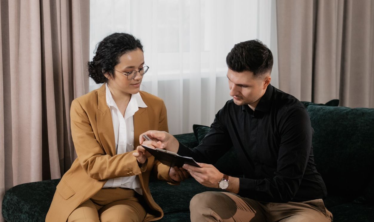 A real estate agent consults with a client, discussing documents in a cozy living room.