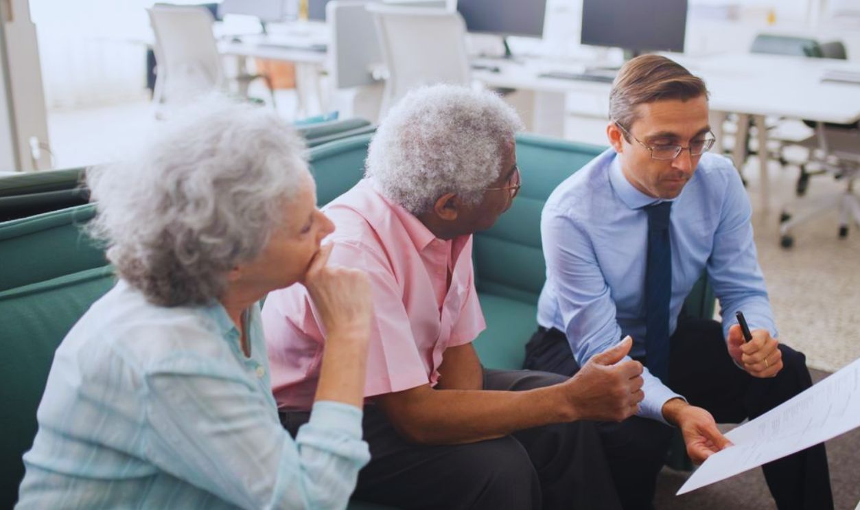 Business professional consults elderly clients in an office setting. Collaborative discussion, paperwork visible