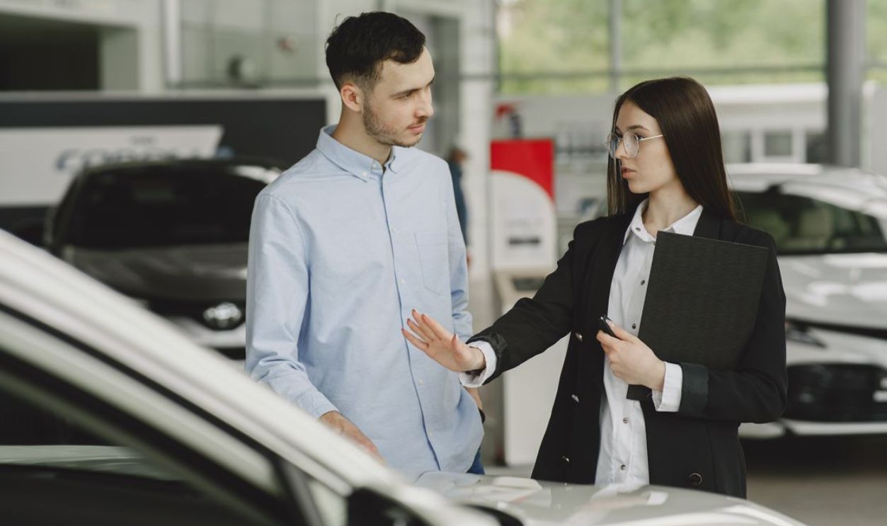A salesperson and customer discussing car features in a dealership setting