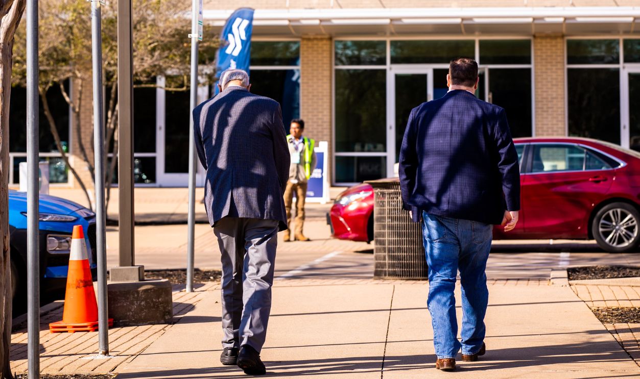 Two adults walking on a sunlit sidewalk in front of a modern building