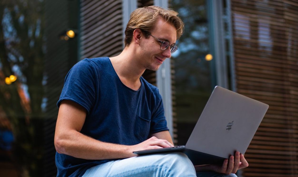 A young man sitting outdoors in Leiden, Netherlands, working on a laptop