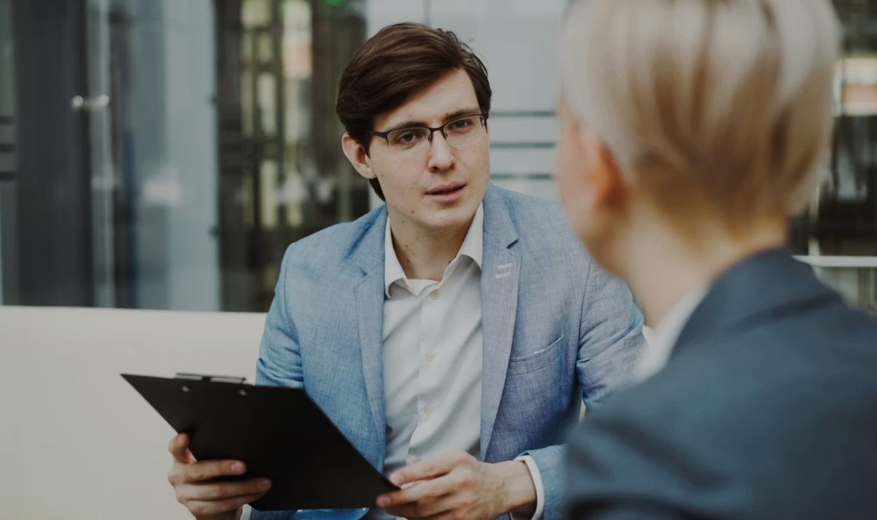 Man in suit holding clipboard talking to woman