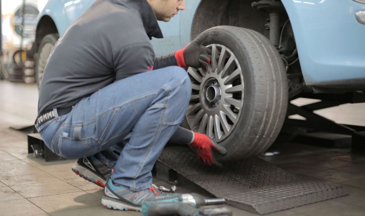 Mechanic changing a car tire indoors, using tools for vehicle maintenance.
