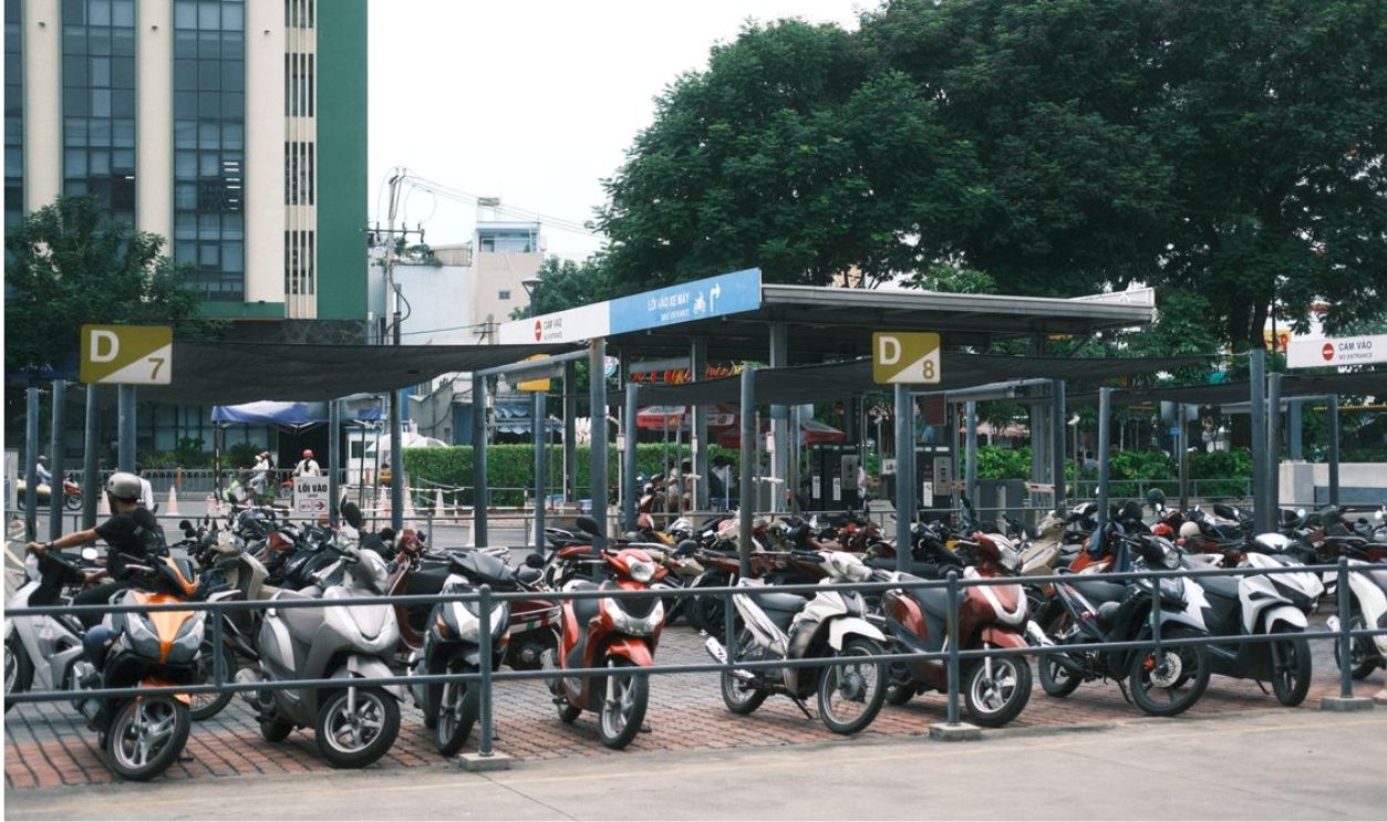 Outdoor motorbike parking area in an urban city setting with multiple parked scooters and bikes.