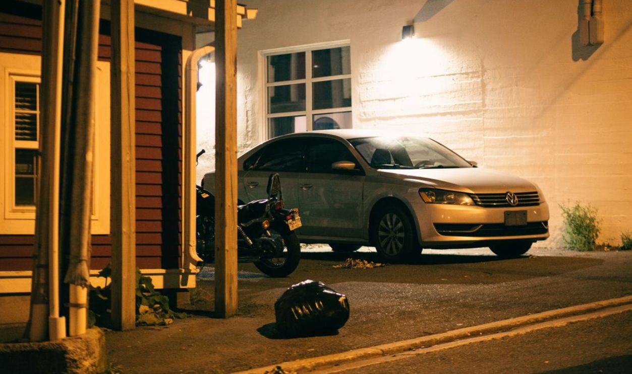 Volkswagen car and motorcycle parked in a dimly lit urban area at night.