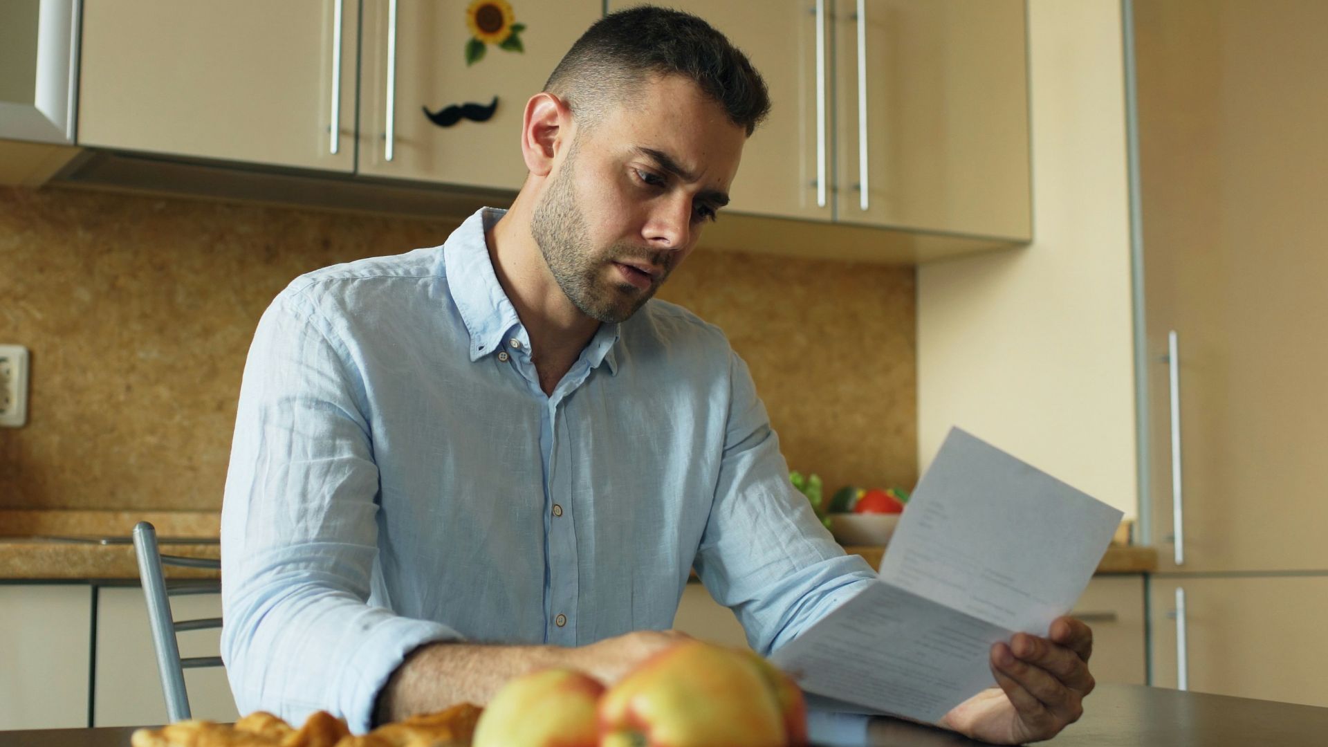 Man reading document at kitchen table with fruit and fruit