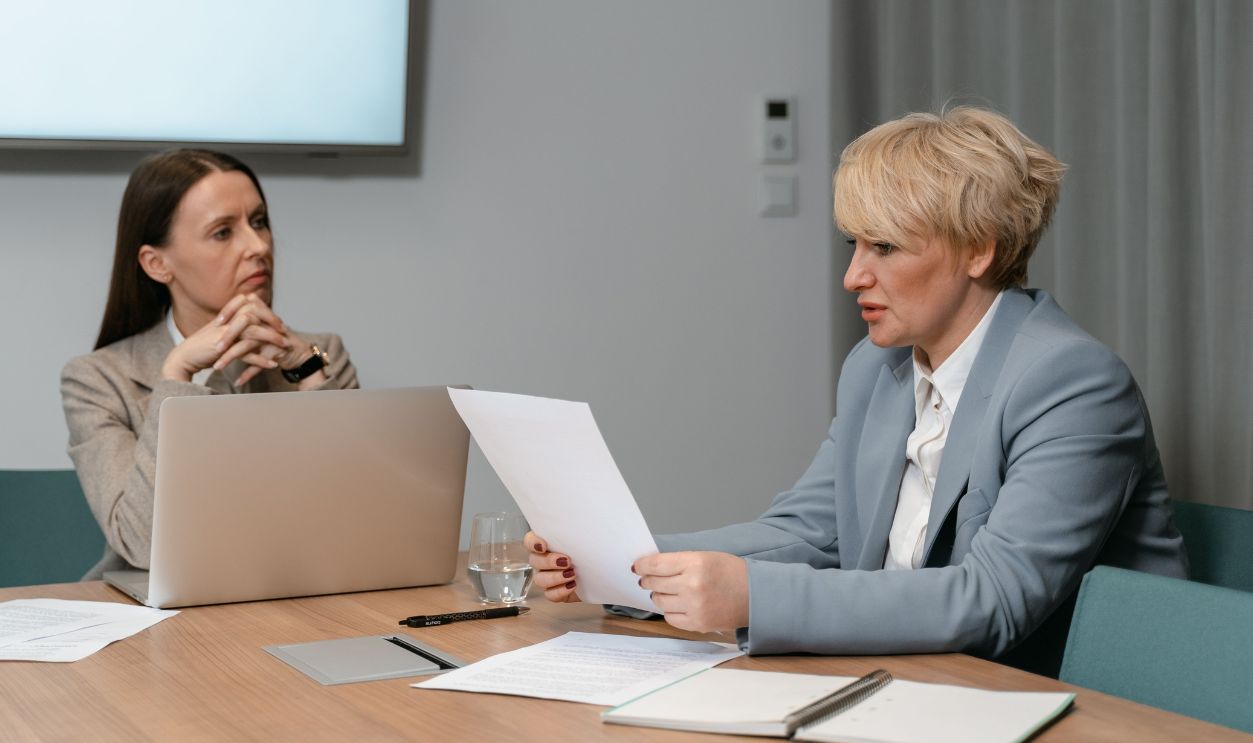 Two businesswomen in a serious meeting, discussing documents with a laptop in an office 