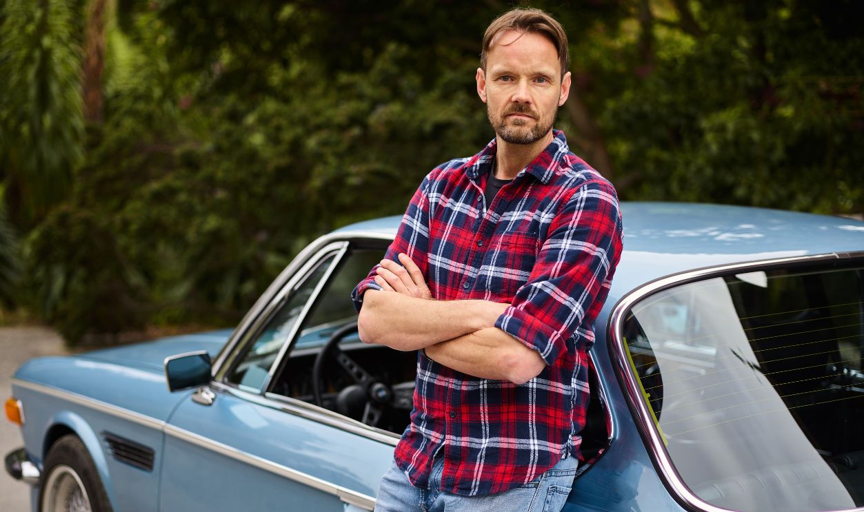 Man with arms crossed leaning on a vintage car