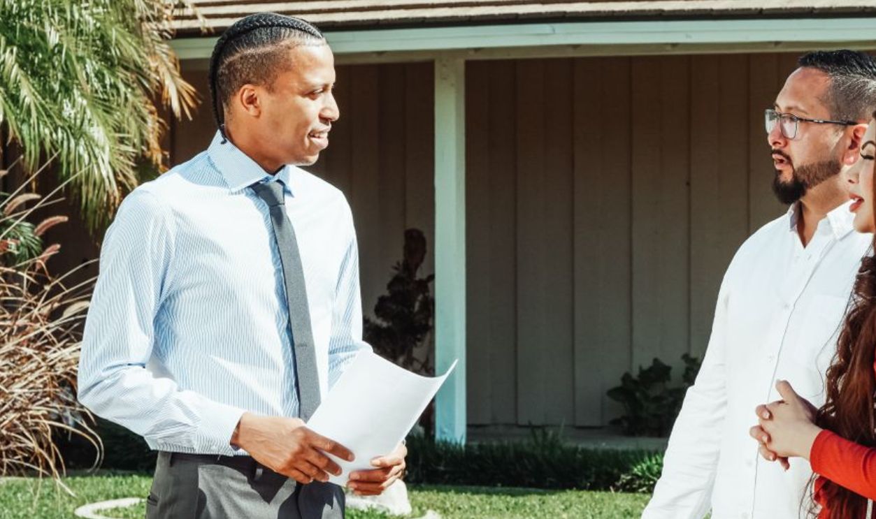 A real estate agent discusses property details with a couple outside a suburban home
