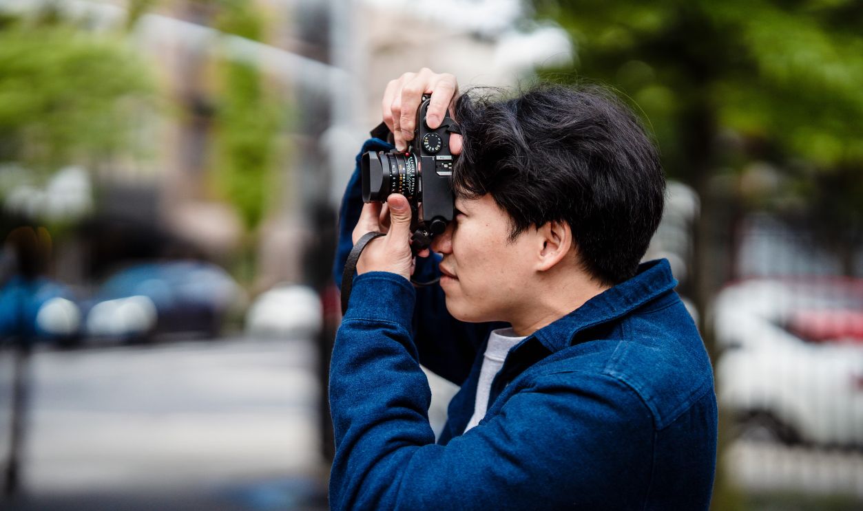 An Asian male photographer takes photos outdoors in an urban setting with a DSLR camera