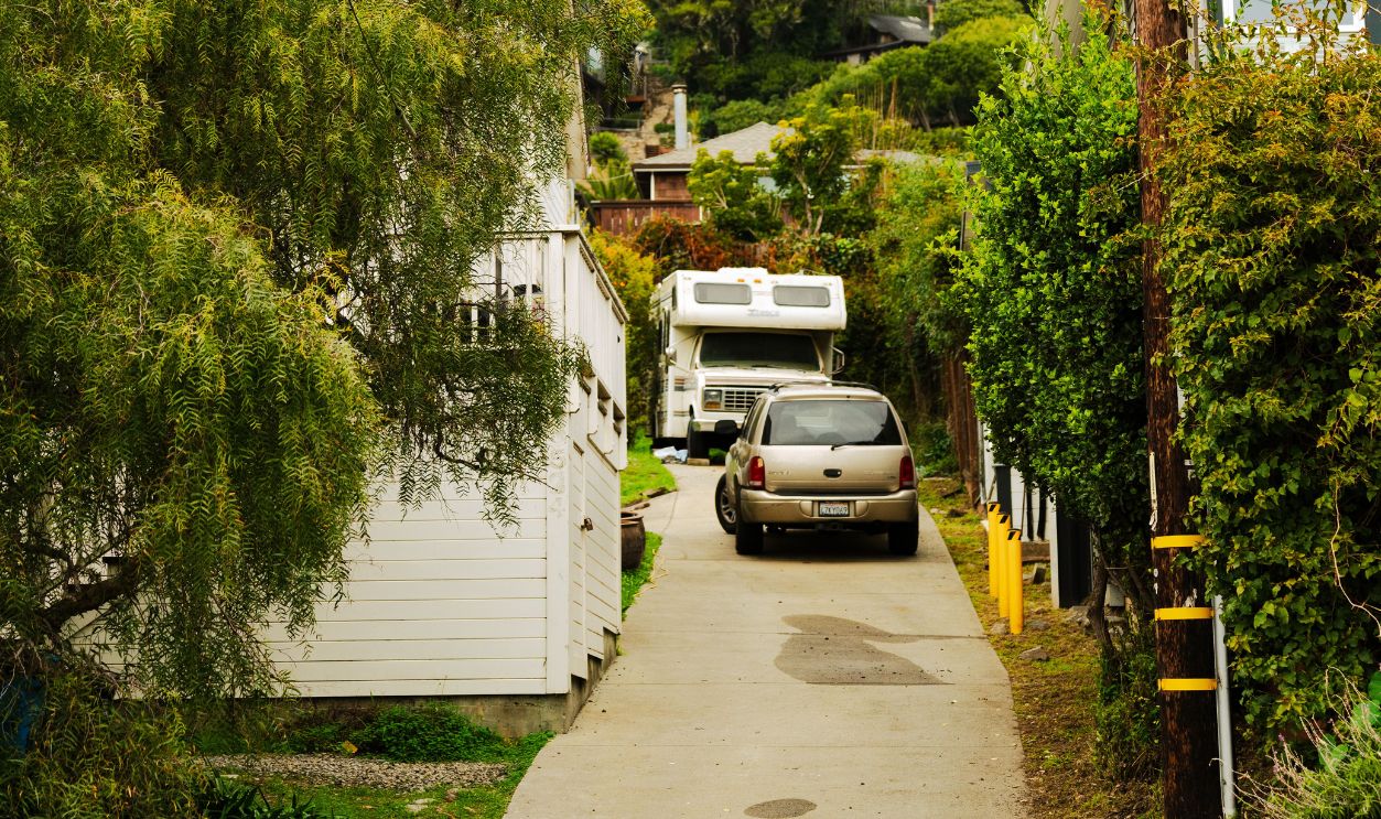 A narrow suburban alleyway lined with greenery and parked vehicles.