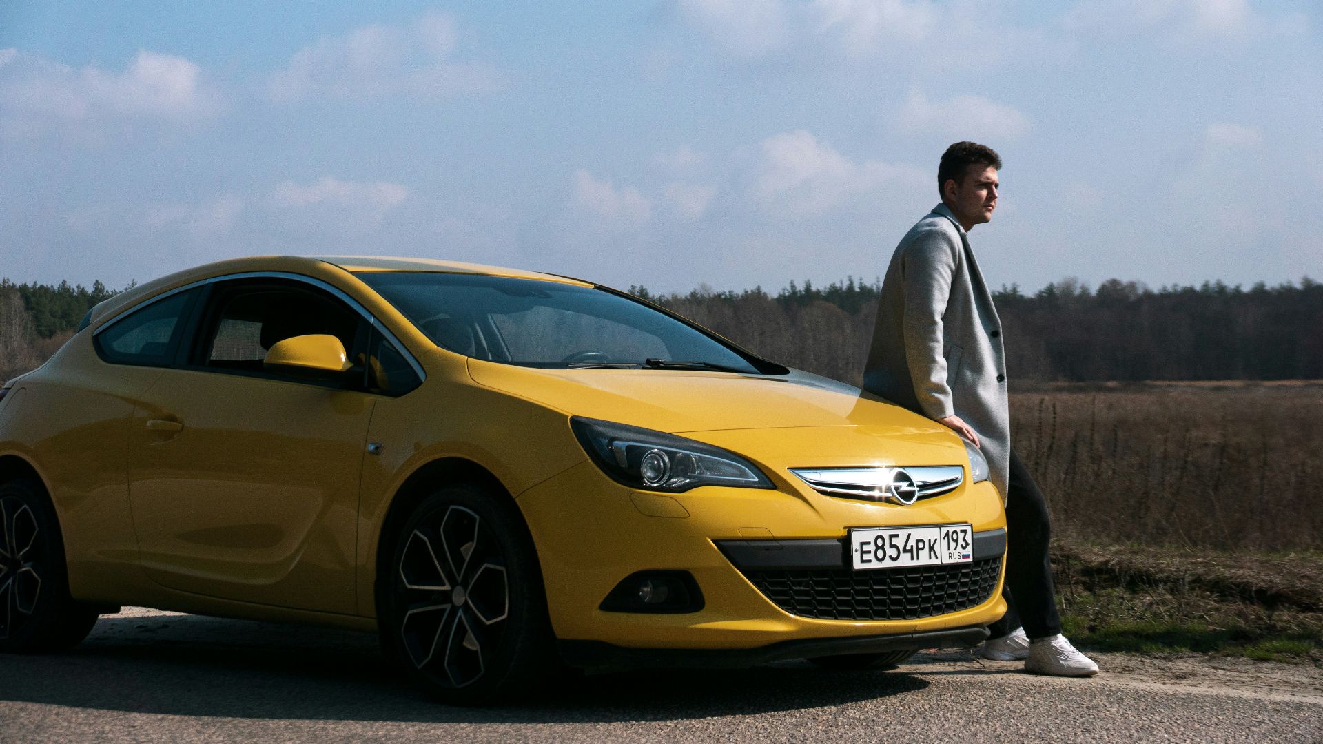 Man poses next to a yellow car.