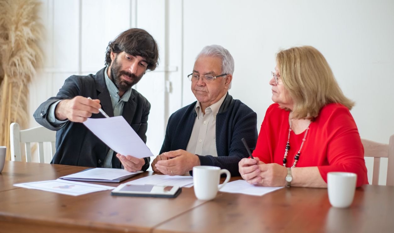 Elderly couple discussing documents with advisor at a wooden table indoors